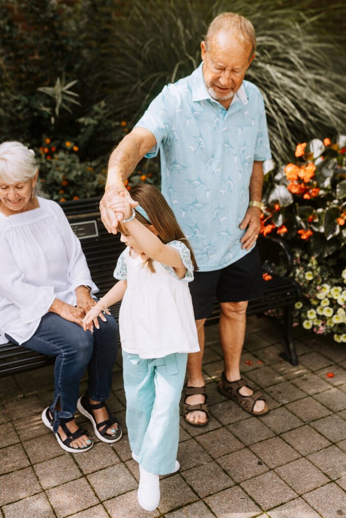 grandparents dancing with granddaughter in front of bush on a sidewalk in Franklin