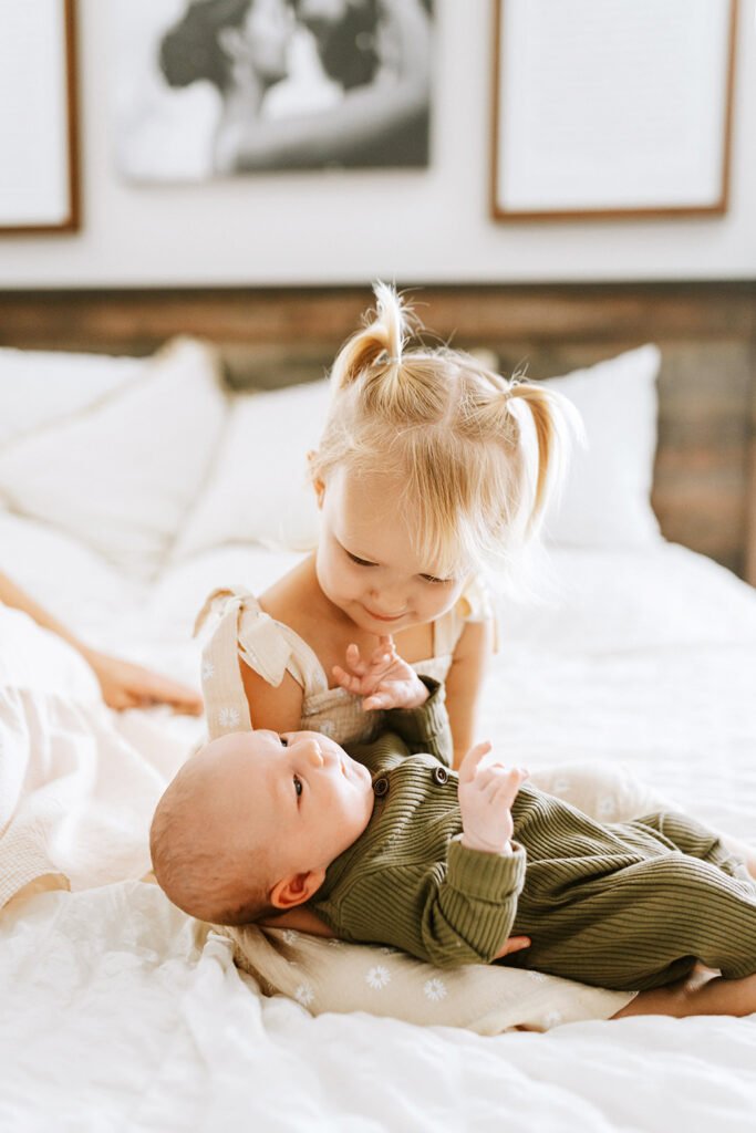 Girl holding a newborn brother bed with white sheet