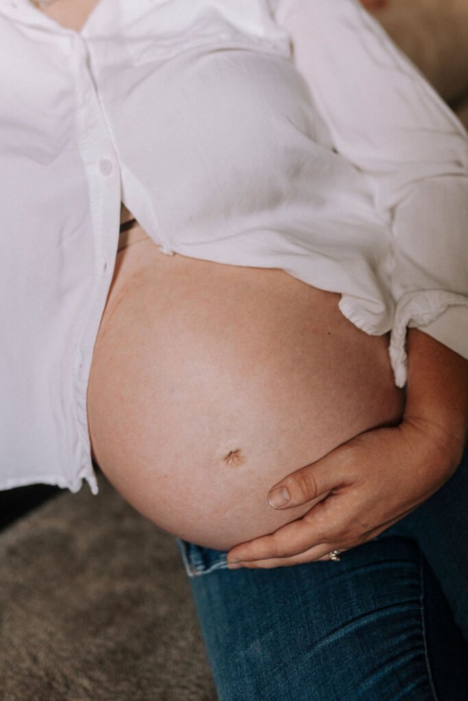 Pregnant woman in white unbuttoned shirt showing baby bump against bare belly