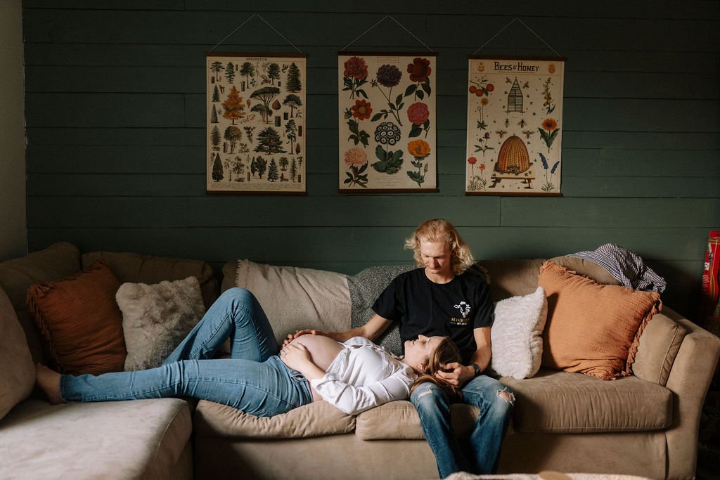 Pregnant couple relaxing together on gray couch in cozy living room setting