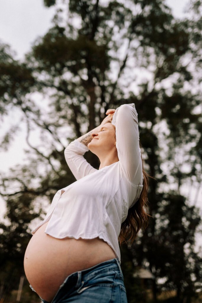 Intimate maternity portrait showing pregnant belly in white unbuttoned shirt and jeans