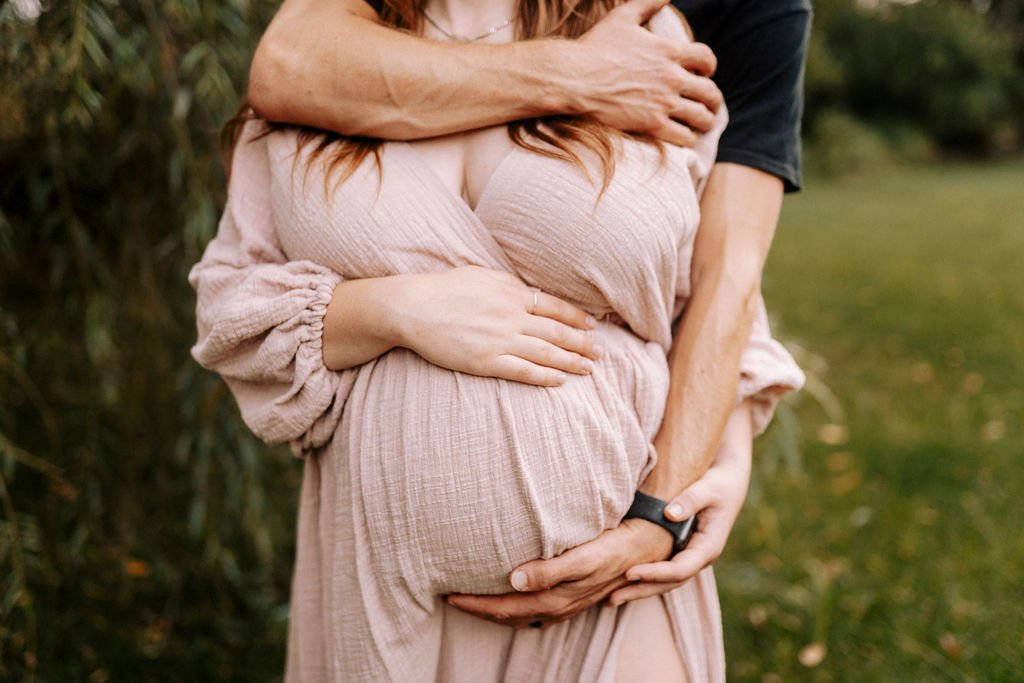 Close-up of expectant couple embracing, showing pregnant belly in flowing beige dress