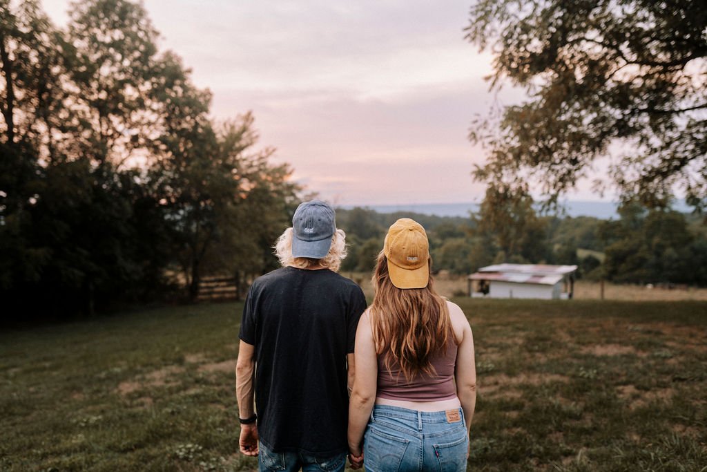 Expectant couple walking away from camera across rural farmland at dusk