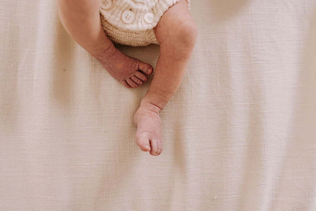 Newborn baby legs in cream knit outfit
