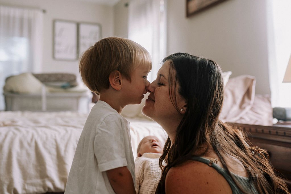 Parents with toddler kissing in bright bedroom during newborn session