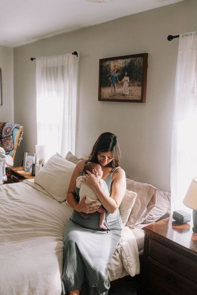 Mother holding newborn baby in cream outfit on bed