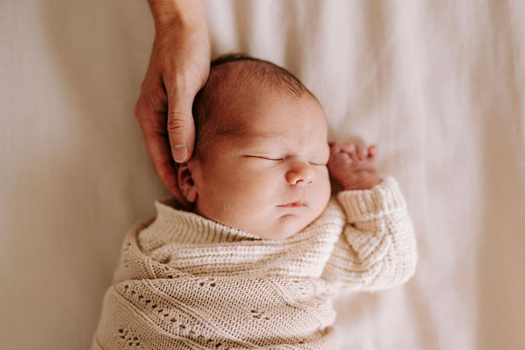 Newborn baby wrapped in cream knit blanket sleeping peacefully
