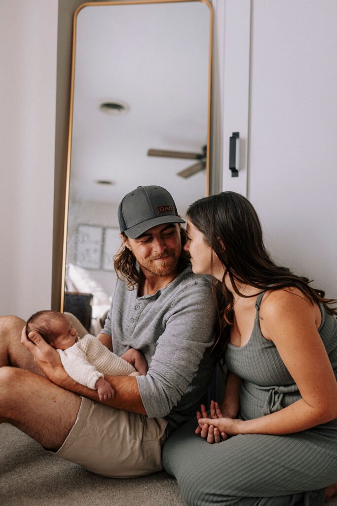Parents cuddling with newborn baby on floor in natural light