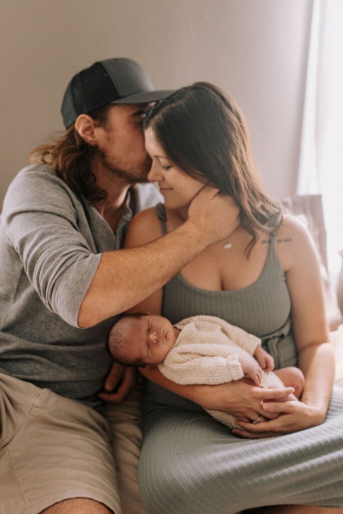 Parents holding newborn baby in cream knit outfit on bed