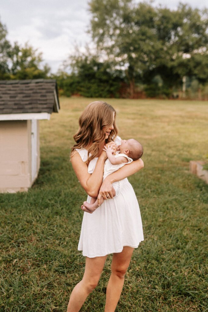 Mom holding newborn while standing in their backyard
