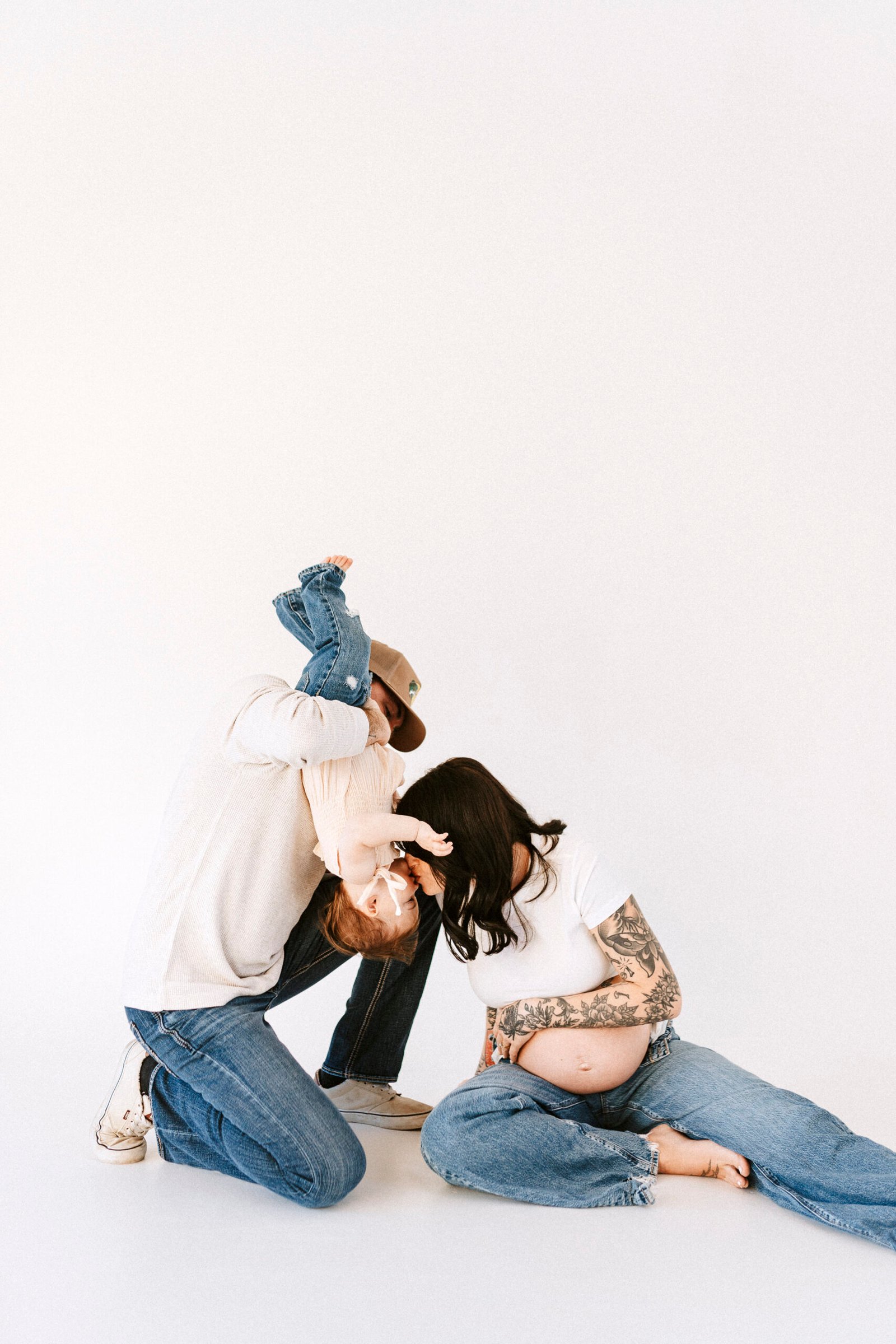 Mom, dad, and daughter playing on an infinity wall during studio maternity session